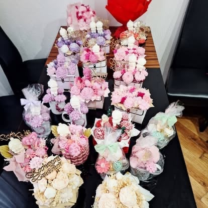 Collection of floral arrangements in various vases and containers displaying pink, white, purple, and red flowers arranged on a black table