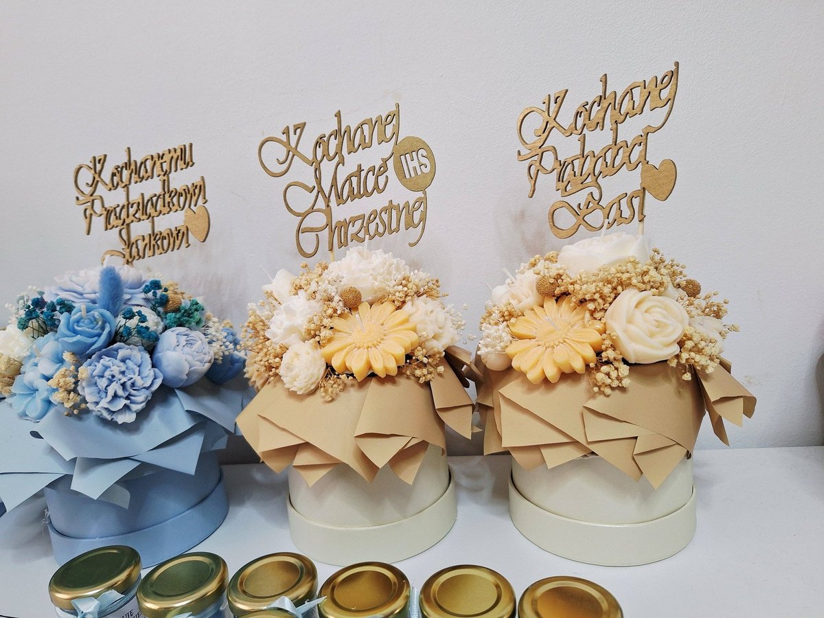 Three decorative floral arrangements in boxes with gold calligraphy signs and wedding rings displayed in front