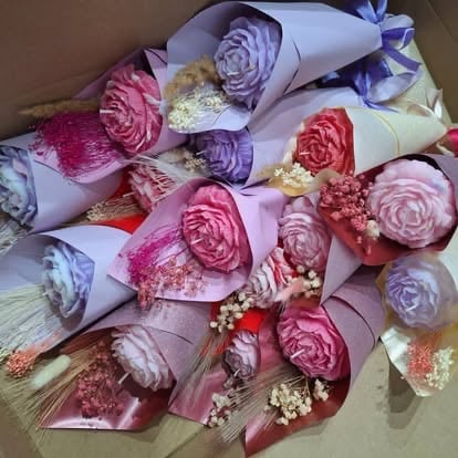 Overhead view of multiple colorful rose bouquets wrapped in pastel paper with babys breath filler flowers arranged on a surface